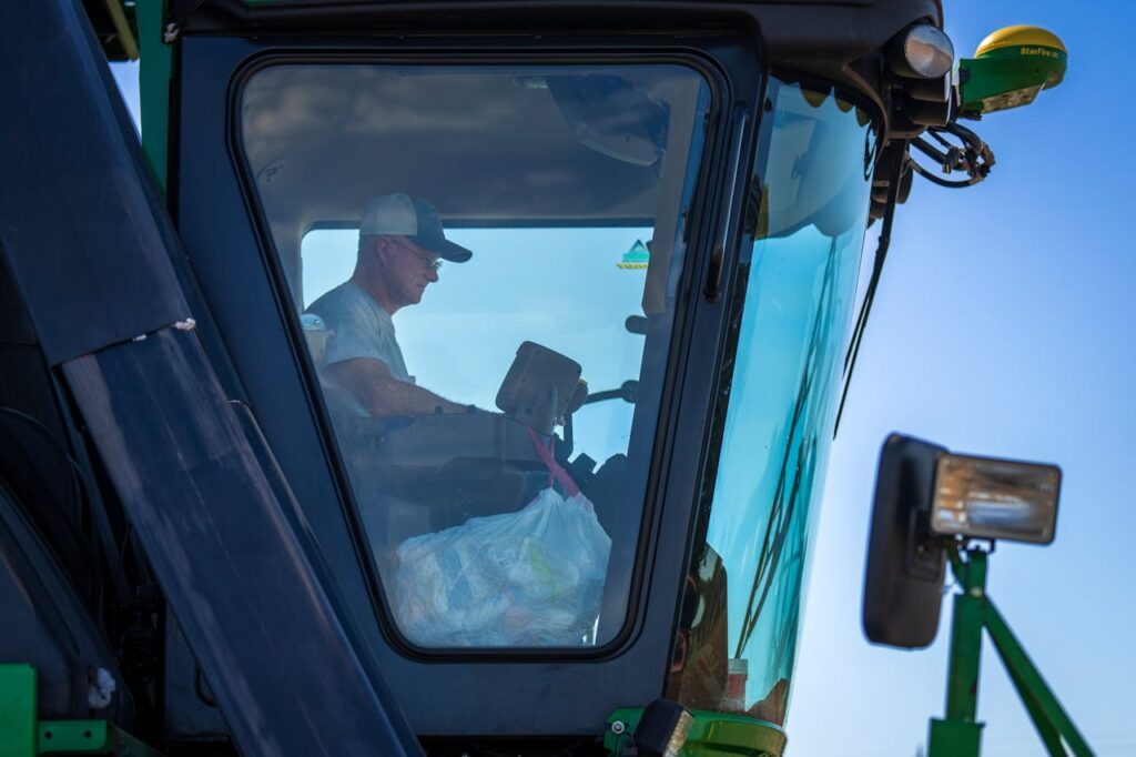A farmer operates a harvester machine from inside the cabin on a clear day.