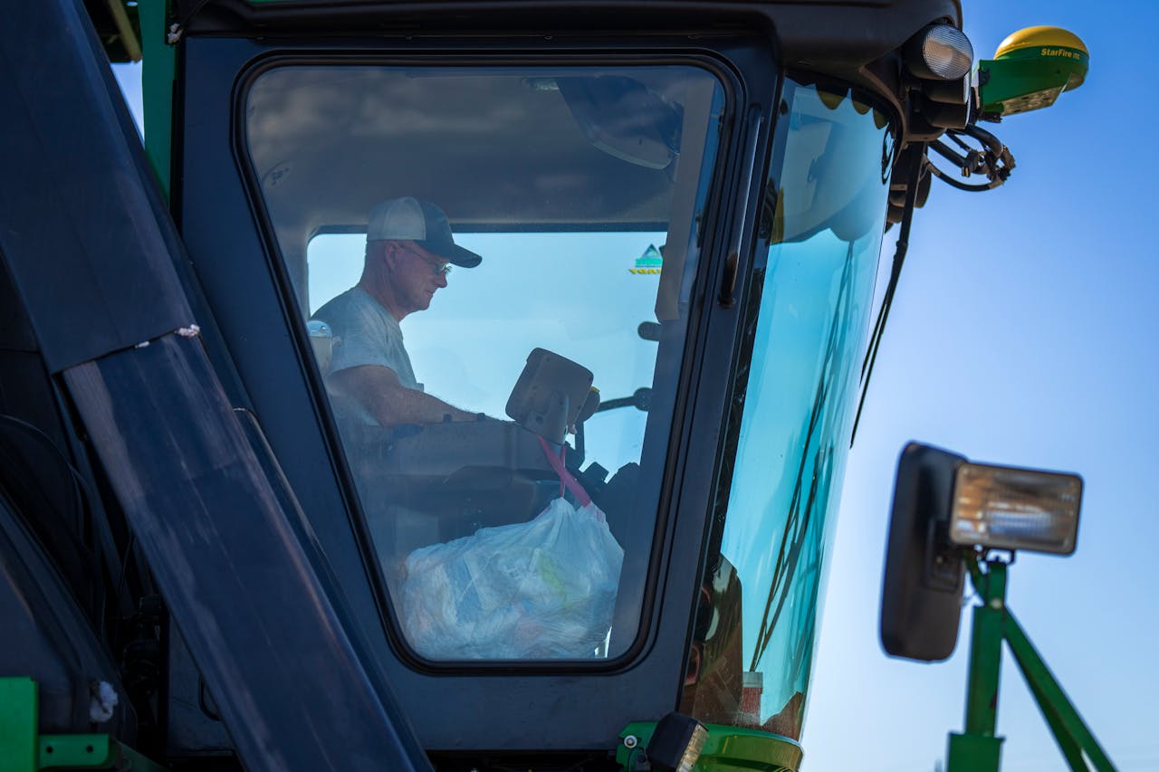 A farmer operates a harvester machine from inside the cabin on a clear day.